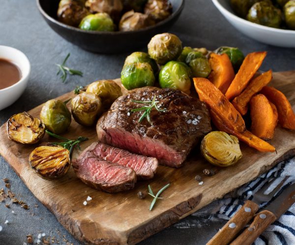 Firefly Lean medium well Steak, Sweet Potato, Roasted Brussels Sprouts_ on a wooden cutting board wi
